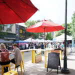 Street fair with pop-up tents and people dining in foreground