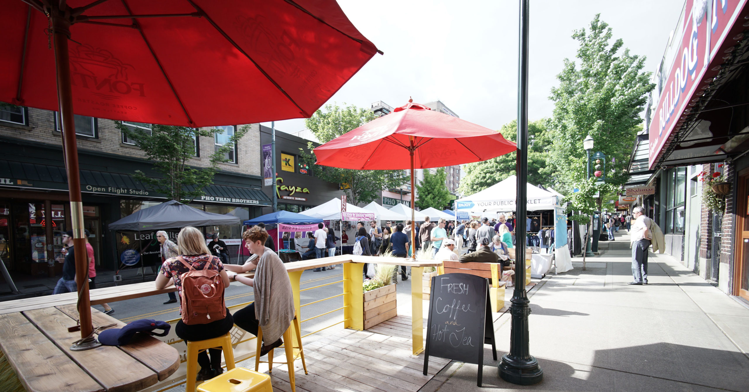 Street fair with pop-up tents and people dining in foreground
